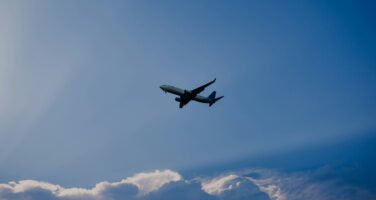 An airplane flying against a bright blue sky with fluffy clouds below.
