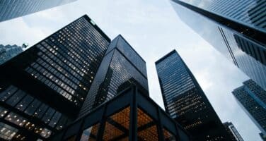 Skyscrapers towering against a cloudy sky, viewed from below, with reflective glass facades highlighting urban architecture.