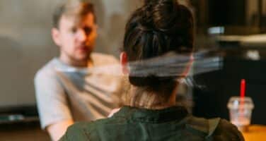 Two people sitting across from each other in a casual office setting, one facing away from the camera.
