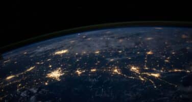 Earth's curve seen from space, illuminated city lights highlight populated areas against the dark atmosphere.