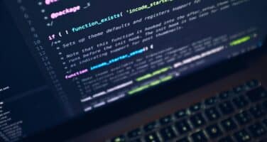 A laptop screen displaying colorful lines of code in a dark theme, focusing on a function definition. The keyboard is partly visible at the bottom, suggesting a programming environment.