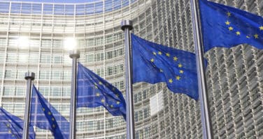 European Union flags waving in front of a glass-fronted building.