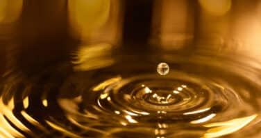 A droplet hovers above golden water ripples, capturing the moment of impact in warm lighting.