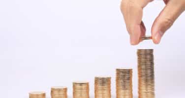 A hand stacking coins in ascending order, creating a visual representation of financial growth on a white background.