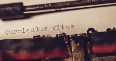 Close-up of a typewriter typing "Curriculum vitae" on a sheet of paper.