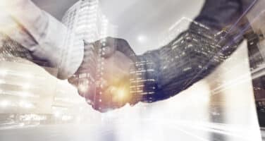 Two people shaking hands with a blurred cityscape in the background, symbolizing business partnership and agreement.