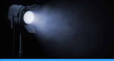 A spotlight shining a bright beam of light through misty air in a dark setting, highlighting the focused intensity of the light.