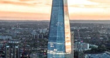 Aerial view of London's skyline at sunset featuring the Shard as a prominent skyscraper, surrounded by other city buildings.