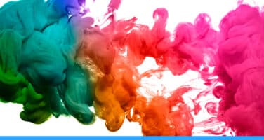 Vibrant clouds of colored ink, including green, blue, orange, red, and pink, swirl and blend together in water against a white background.