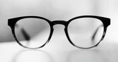 Black-framed eyeglasses centered on a white surface, with a blurred background.
