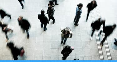 Aerial view of people walking in various directions on a tiled floor, creating a sense of busy movement.