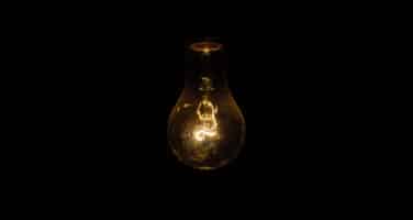 A dimly lit incandescent light bulb glowing softly against a dark background.