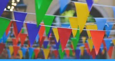 Colorful triangular pennant flags strung across an outdoor setting, featuring vivid blue, red, yellow, and green hues.