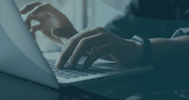 Hands typing on a laptop keyboard in a dimly lit setting, conveying a sense of focus and productivity.