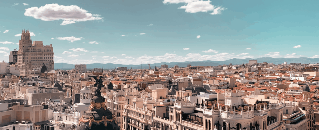 Panoramic view of Madrid's cityscape under a clear blue sky, featuring historic buildings and distant mountains in the background.