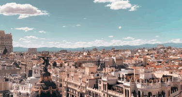 Panoramic view of Madrid's cityscape under a clear blue sky, featuring historic buildings and distant mountains in the background.