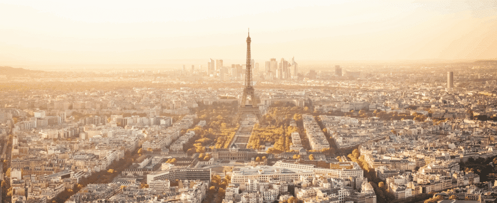 Aerial view of Paris at sunset with the Eiffel Tower in the center, surrounded by city buildings and distant skyline.