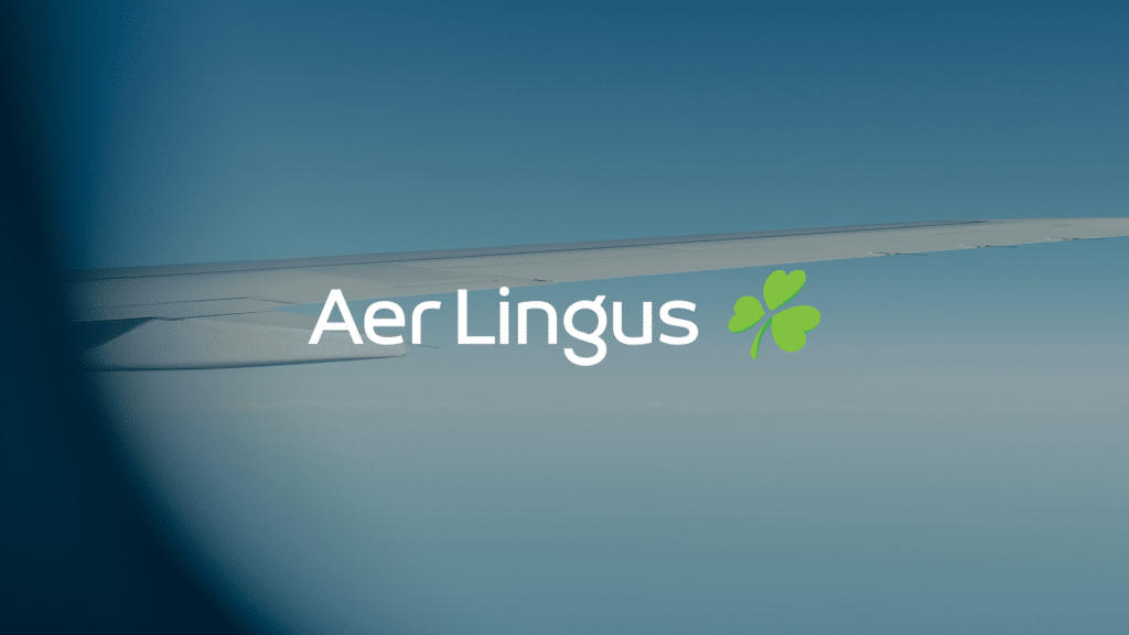 Aer Lingus logo featuring the airline's name in white with a green shamrock icon, set against a blurred background of an airplane wing and blue sky.