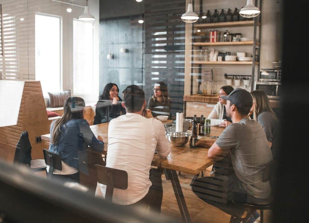 A group of people sitting around a wooden table in a casual meeting room, discussing collaboratively.