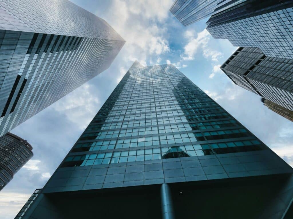 Looking up at a group of modern skyscrapers against a partly cloudy sky, emphasizing their height and sleek architecture.