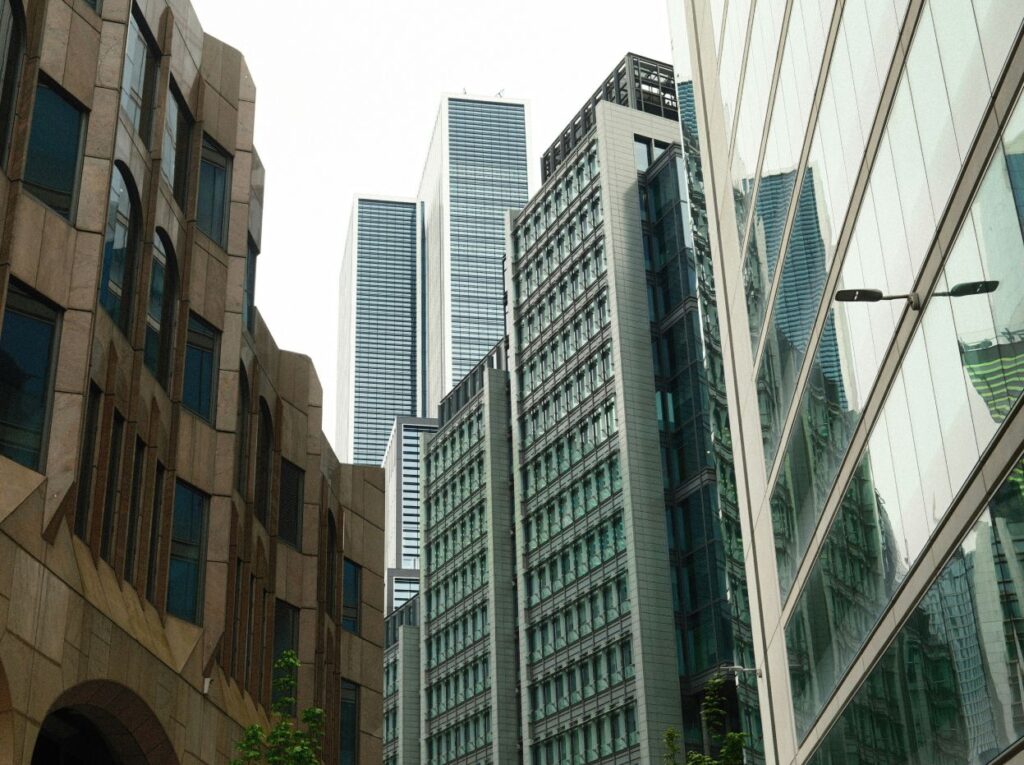 Modern urban scene with diverse skyscrapers, featuring glass and stone facades, against an overcast sky.