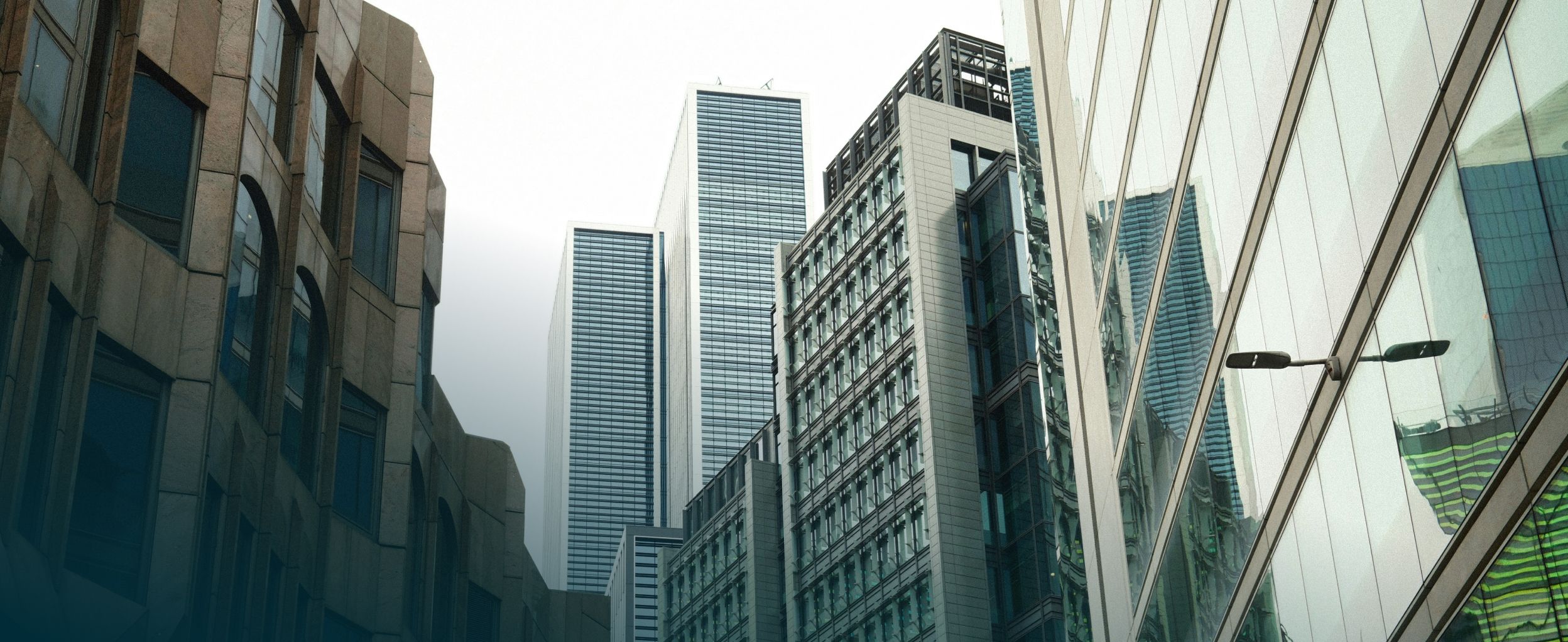 Tall modern office buildings with glass facades rise against a cloudy sky, creating an urban cityscape.