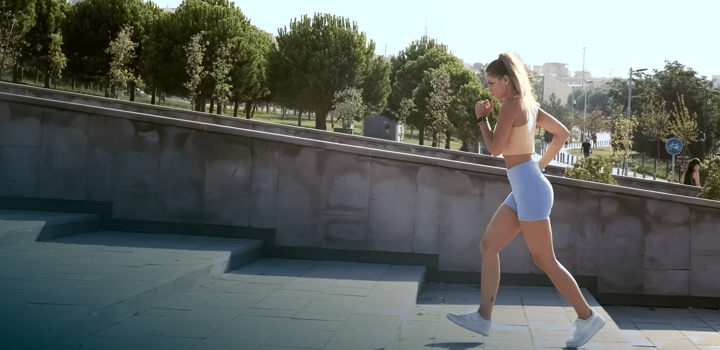 A woman in athletic wear runs up outdoor stairs surrounded by greenery.