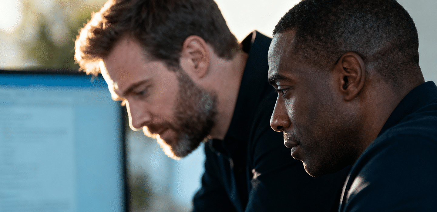 Two men focused on a computer screen, working closely together, in an office environment.