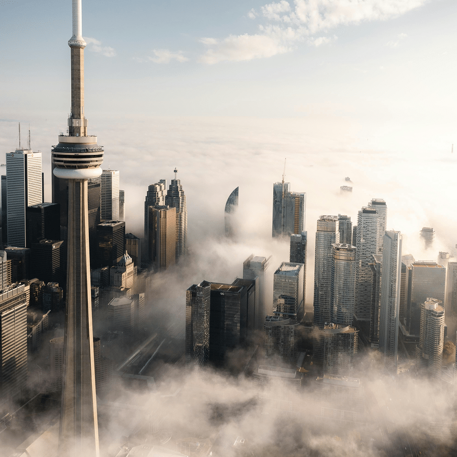 Aerial view of Toronto's skyline with the CN Tower rising above buildings surrounded by low-lying clouds.