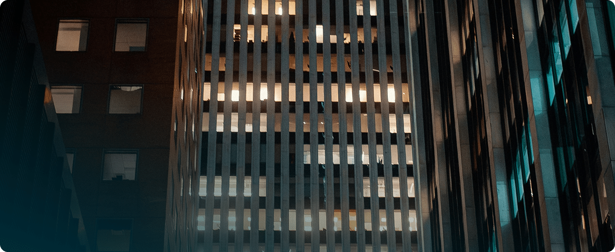 Tall office buildings at night with lit windows, reflecting an urban cityscape.
