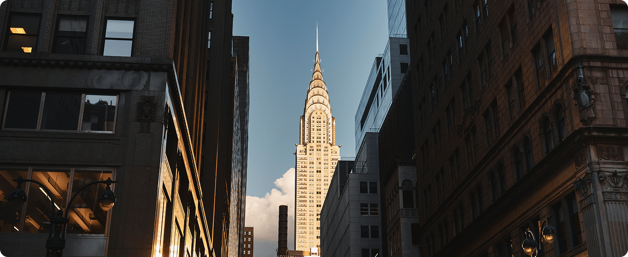 View of the Chrysler Building framed by surrounding dark buildings, with a clear blue sky in the background.