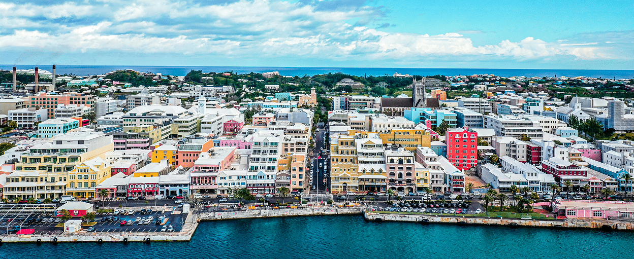 Aerial view of Hamilton, Bermuda, showcasing colorful buildings along the waterfront, clear blue skies, and a calm harbor.
