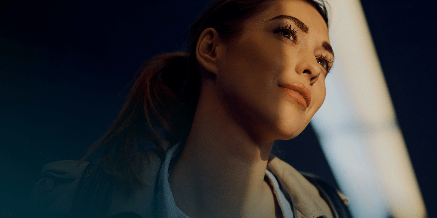 A woman gazes upward with a soft smile, illuminated by warm, ambient lighting against a dark background.