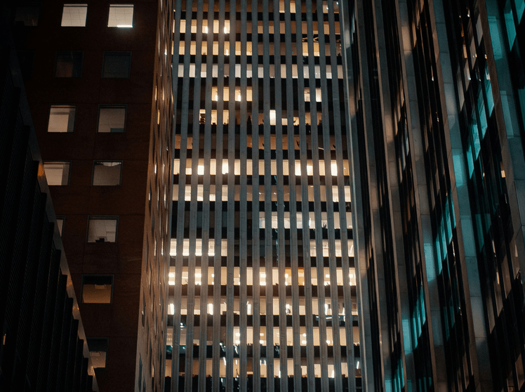 Tall city buildings at night with illuminated windows, showcasing urban life and activity.